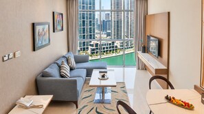 A modern living room with a sofa, a dining table, and a view of a cityscape through large windows. - Canal Central Hotel Business Bay (Dubai)