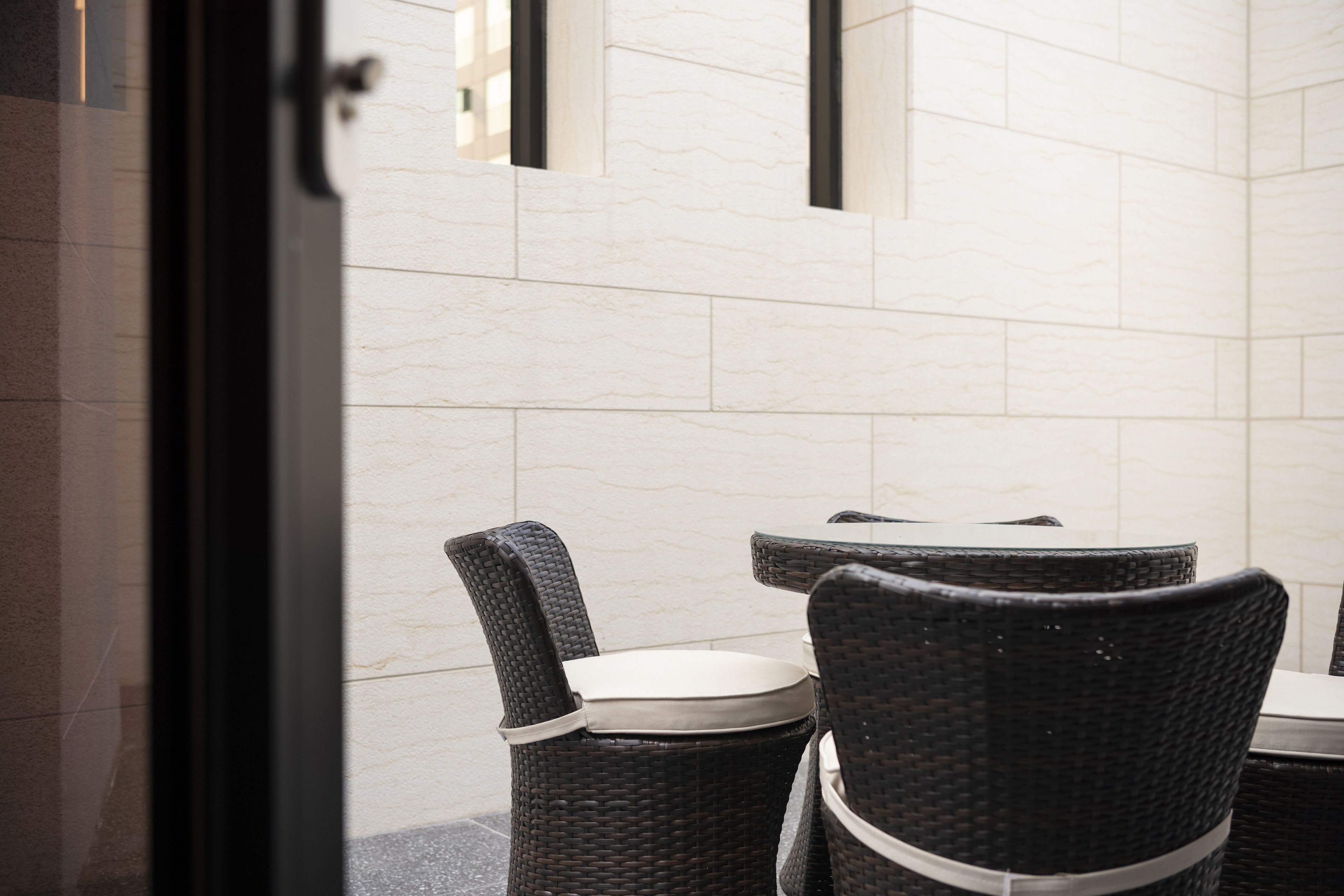 A view of a dining area with wicker chairs and a table, a tiled wall, and a door frame.