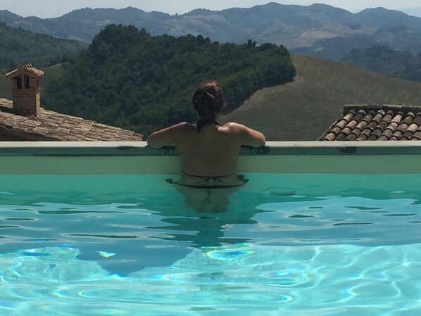 A person in a swimming pool with a view of hills and a small building in the background.