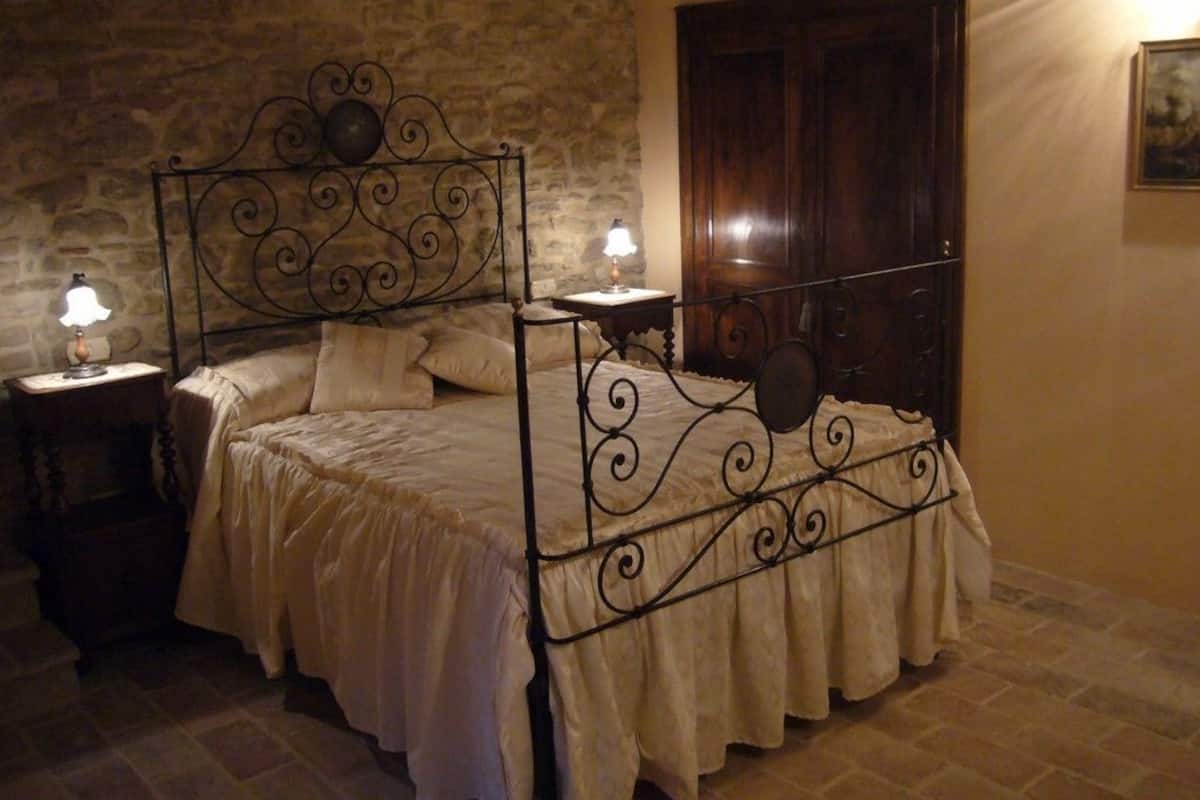 Une chambre à coucher avec un lit en fer forgé, un mur en pierre, une porte en bois et un tableau accroché au mur.