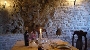 Zona de dinar amb parets de pedra, taula preparada per a dues persones, amb espelma, ampolla de vi i coberts.