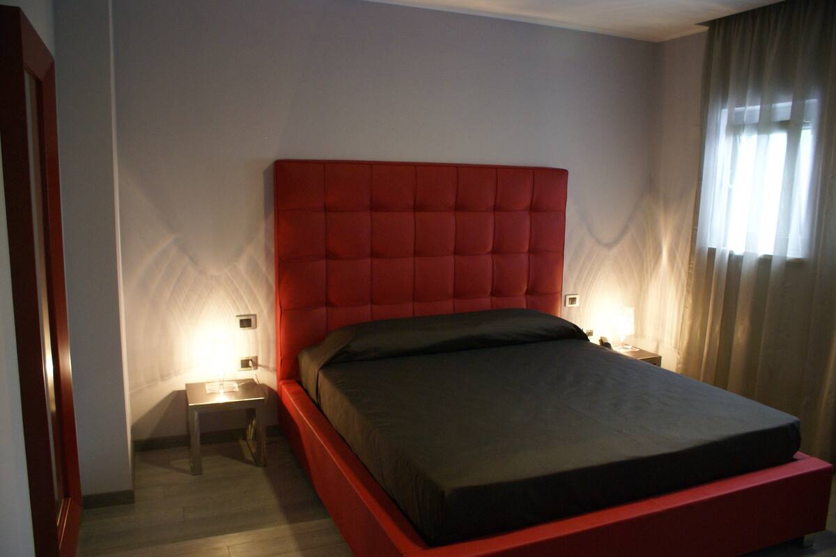 A modern bedroom with a red headboard, a single bed, a nightstand, and a lamp.