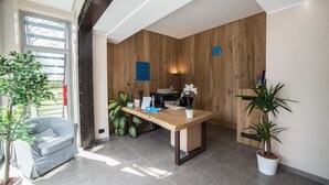 Una moderna zona de recepción con una pared de madera, un mostrador de recepción, un letrero azul y plantas en macetas.