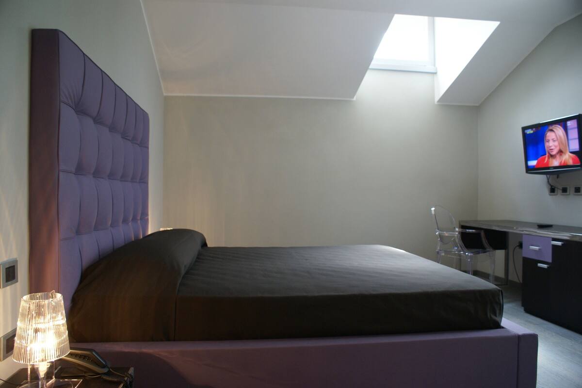 A modern bedroom with a large bed, a desk, a television, and a skylight.