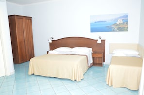 Un dormitorio con una cama doble, una cama individual, un armario de madera y un cuadro de un paisaje costero.