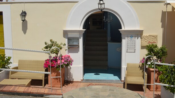 A hotel entrance with a white archway, a staircase, and two wicker chairs with potted plants. - Borgo800 (San Nicola Arcella)