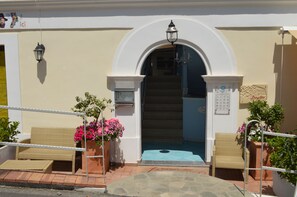 A hotel entrance with a white archway, a staircase, and two wicker chairs with potted plants. - Borgo800 (San Nicola Arcella)