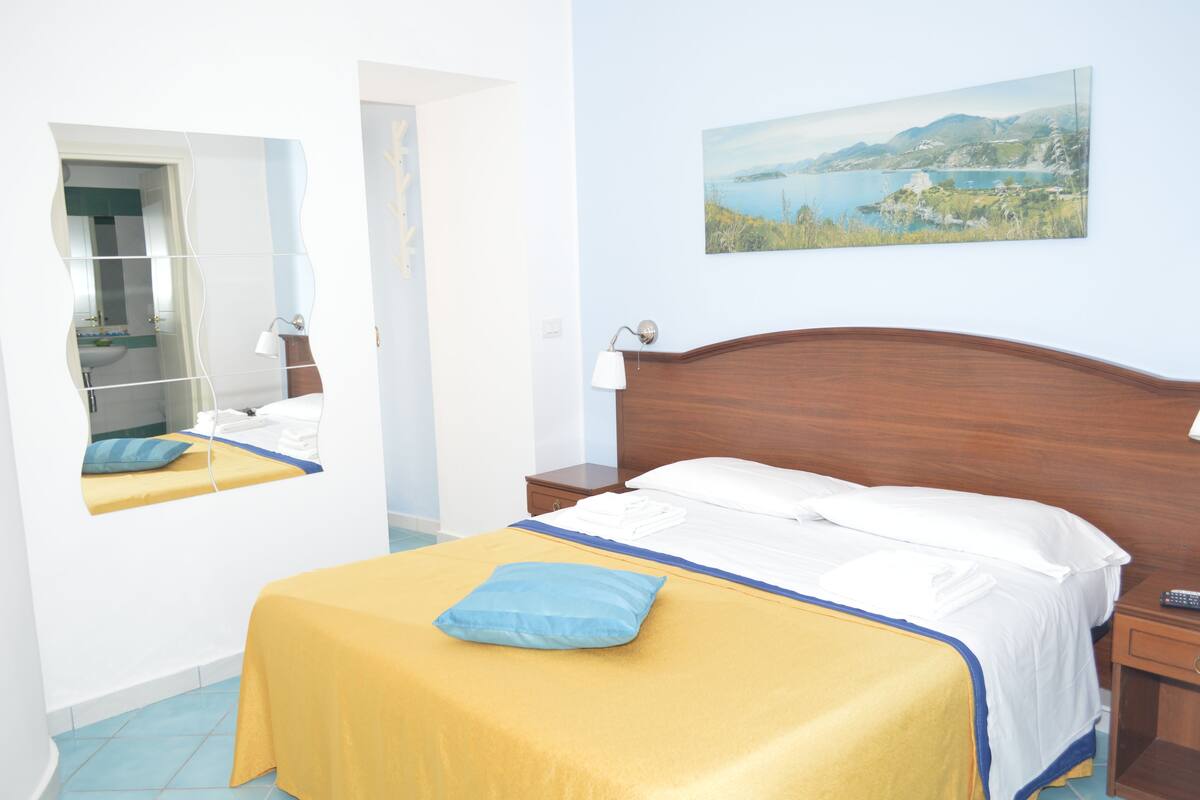 Ein Hotelzimmer mit Bett, Nachttisch, Spiegel und einem Bild an der Wand.