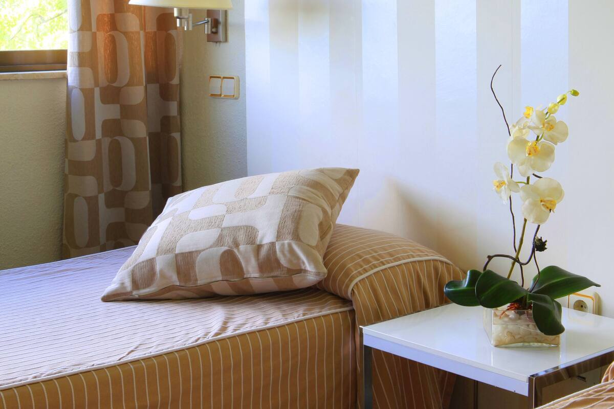 A hotel room with two beds, a nightstand, a lamp, and a window with curtains.