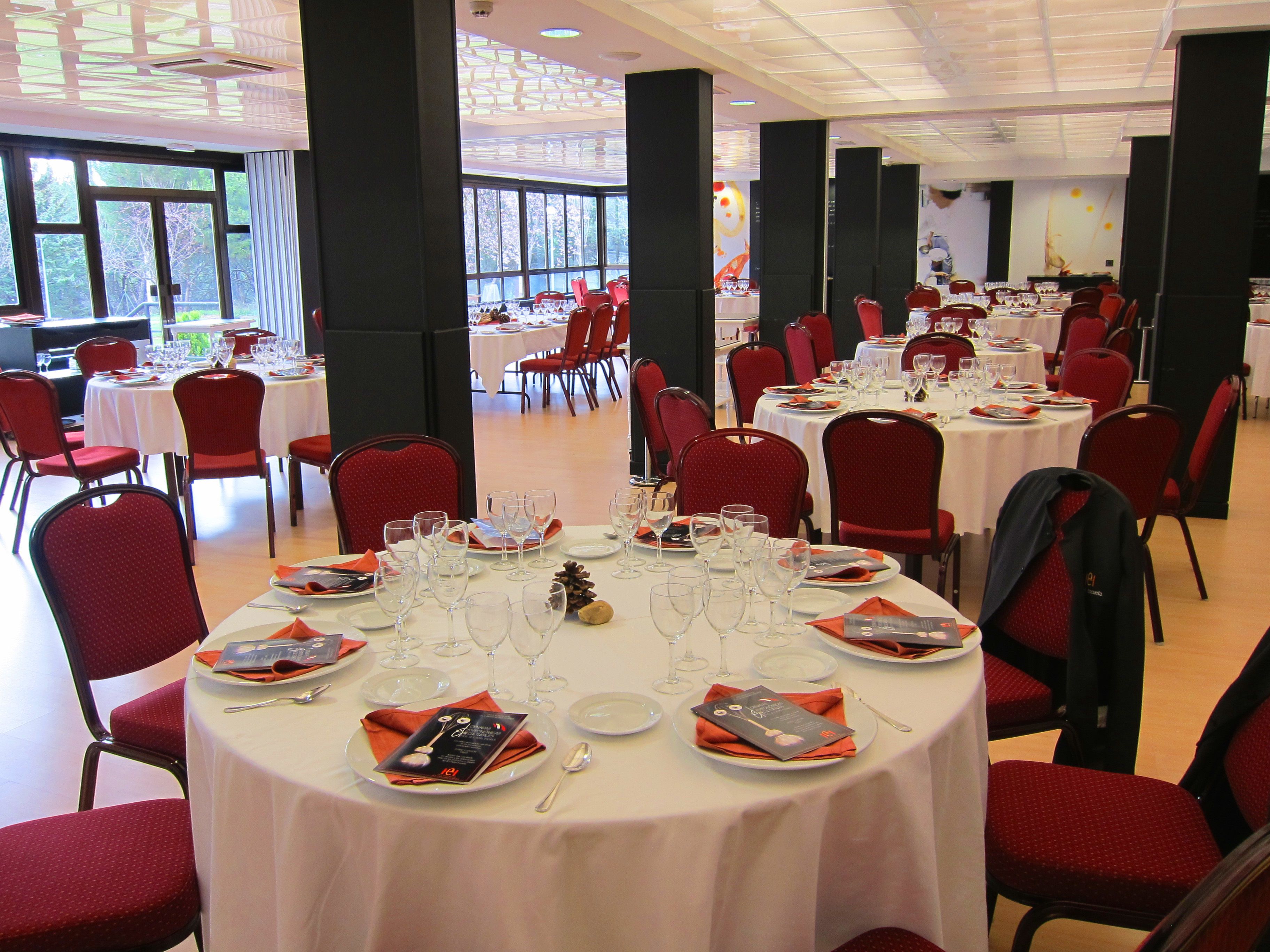 Un salón de banquetes con mesas redondas dispuestas para comer, sillas rojas y vistas al exterior a través de amplios ventanales.