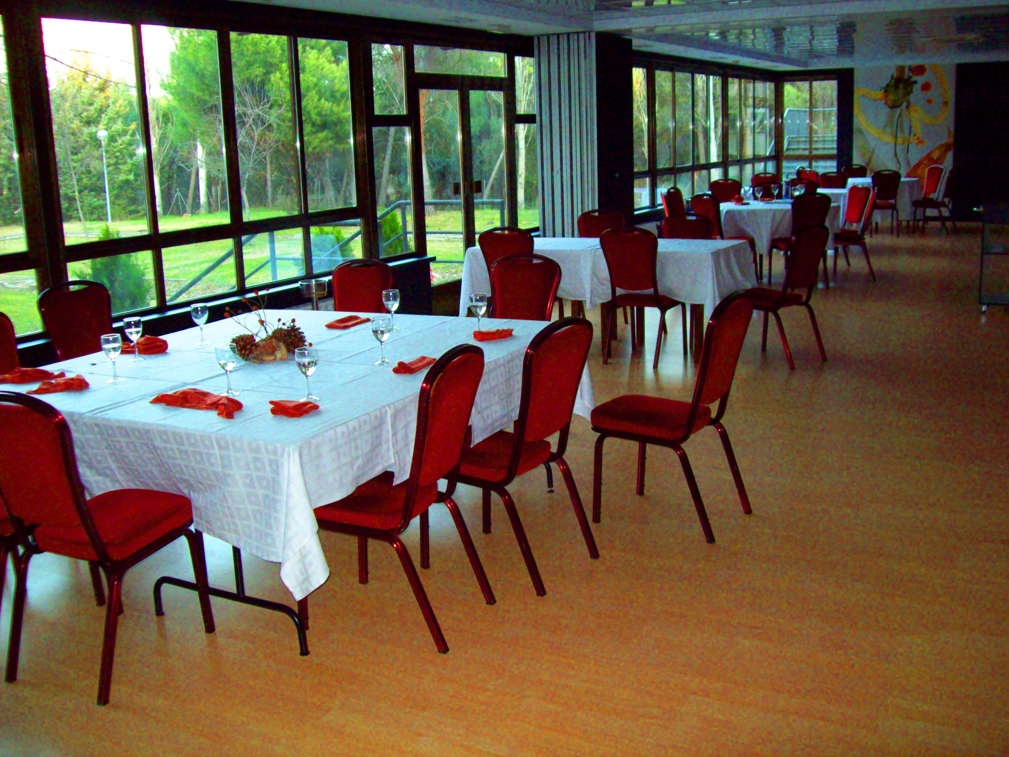 Un comedor con mesas dispuestas para una comida, ventanas amplias y vistas al exterior.