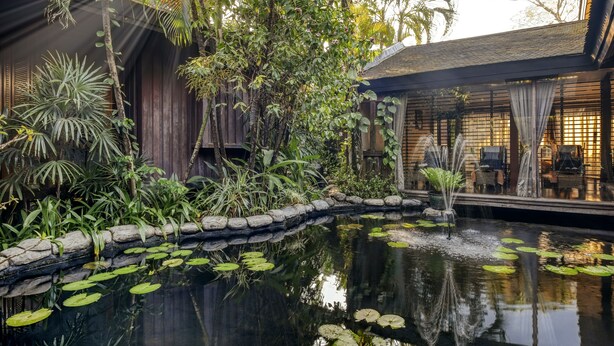 Un jardin intérieur paisible, avec un bassin, une végétation luxuriante et des structures en bois.
