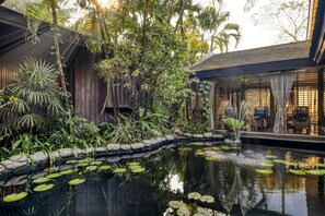 Ein ruhiger Innenhofgarten mit Teich, üppiger Bepflanzung und Holzelementen.