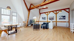A spacious loft with high ceilings, exposed wooden beams, a dining area with a white table and chairs, a seating area with sofas, and artwork on the walls. - Apartment Senftenberg - 1907 (Senftenberg)