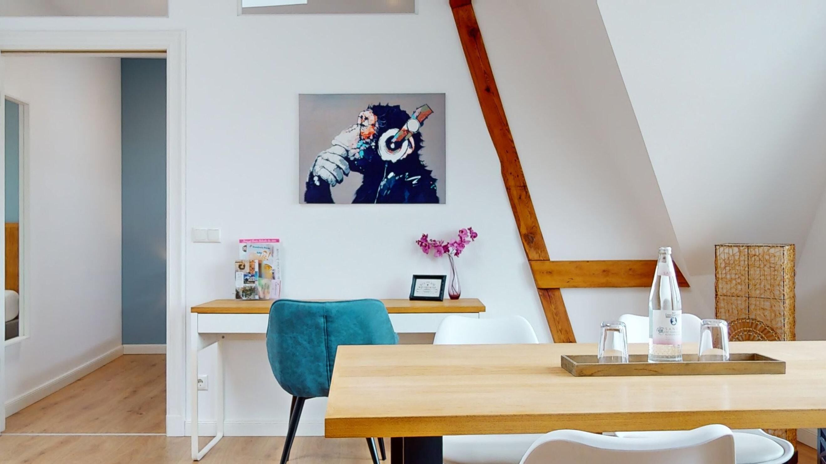 Una habitación moderna y bien iluminada con un escritorio de madera, una silla color turquesa y un cuadro en la pared.