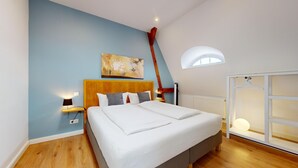 A bedroom with a bed, a wooden headboard, a painting, a window, and a radiator. - Apartment Senftenberg - 1907 (Senftenberg)