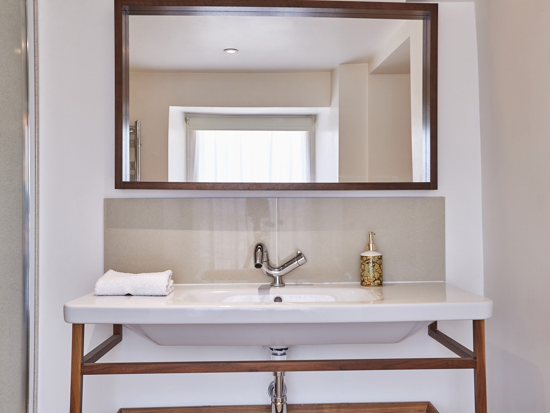 Un baño con un lavamanos blanco, un espejo y una toalla.
