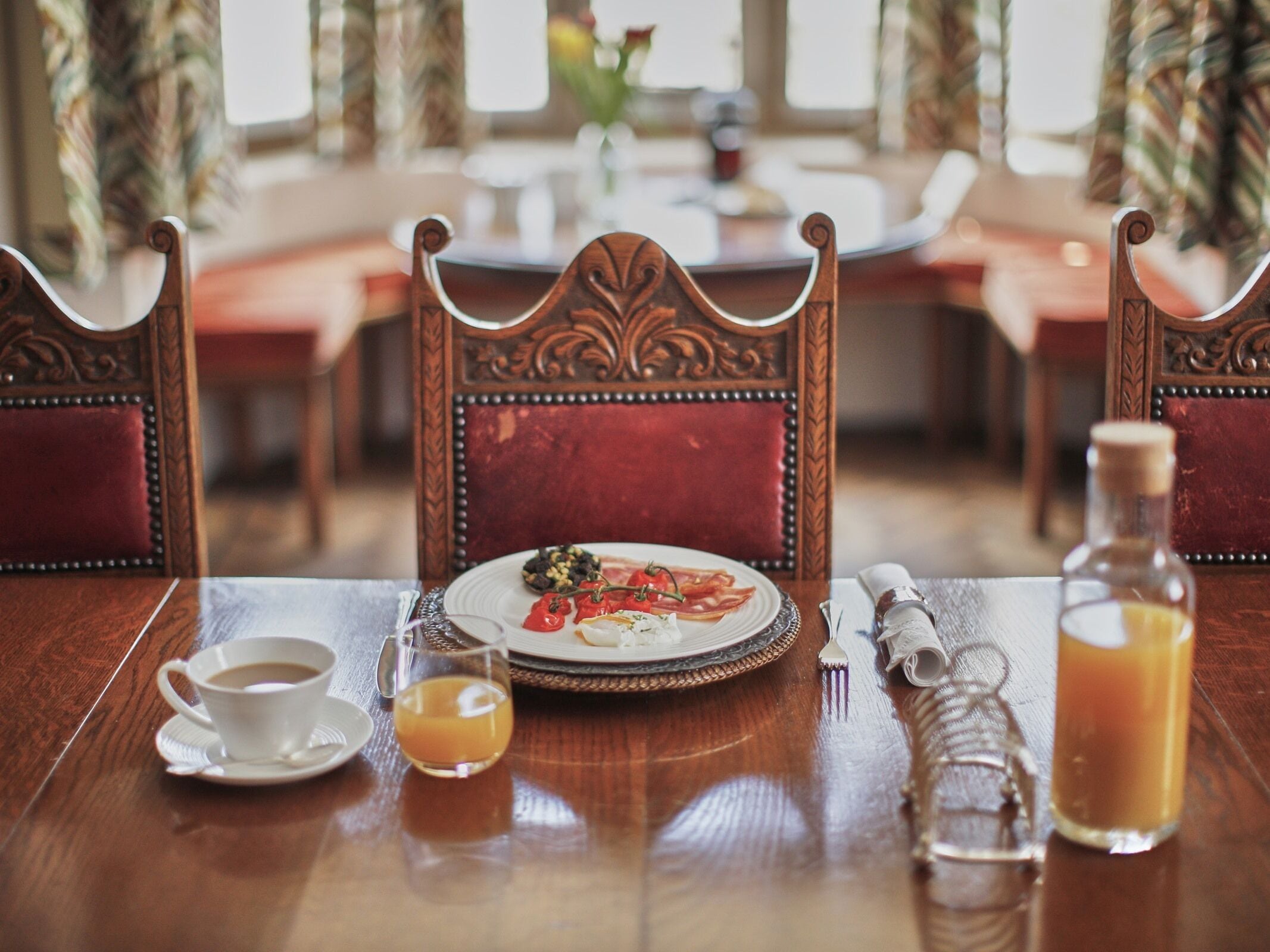 A dining table with a plate of food, a cup of coffee, a glass of orange juice, and a bottle of juice.