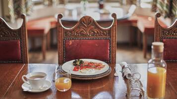 A dining table with a plate of food, a cup of coffee, a glass of orange juice, and a bottle of juice.