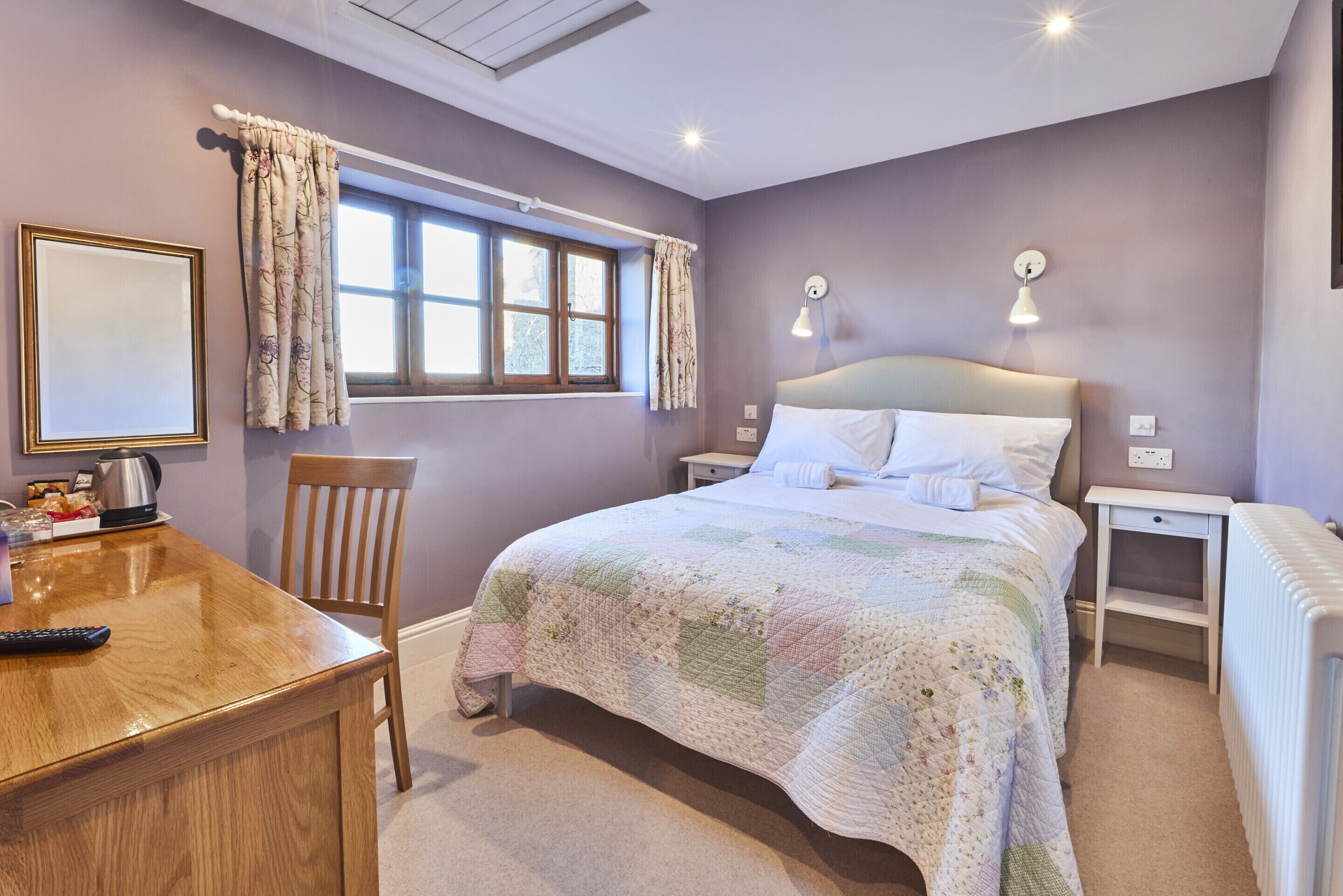 A bedroom with a bed, bedside tables, a chair, a desk, and a window with curtains.