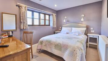 A bedroom with a bed, bedside tables, a chair, a desk, and a window with curtains.