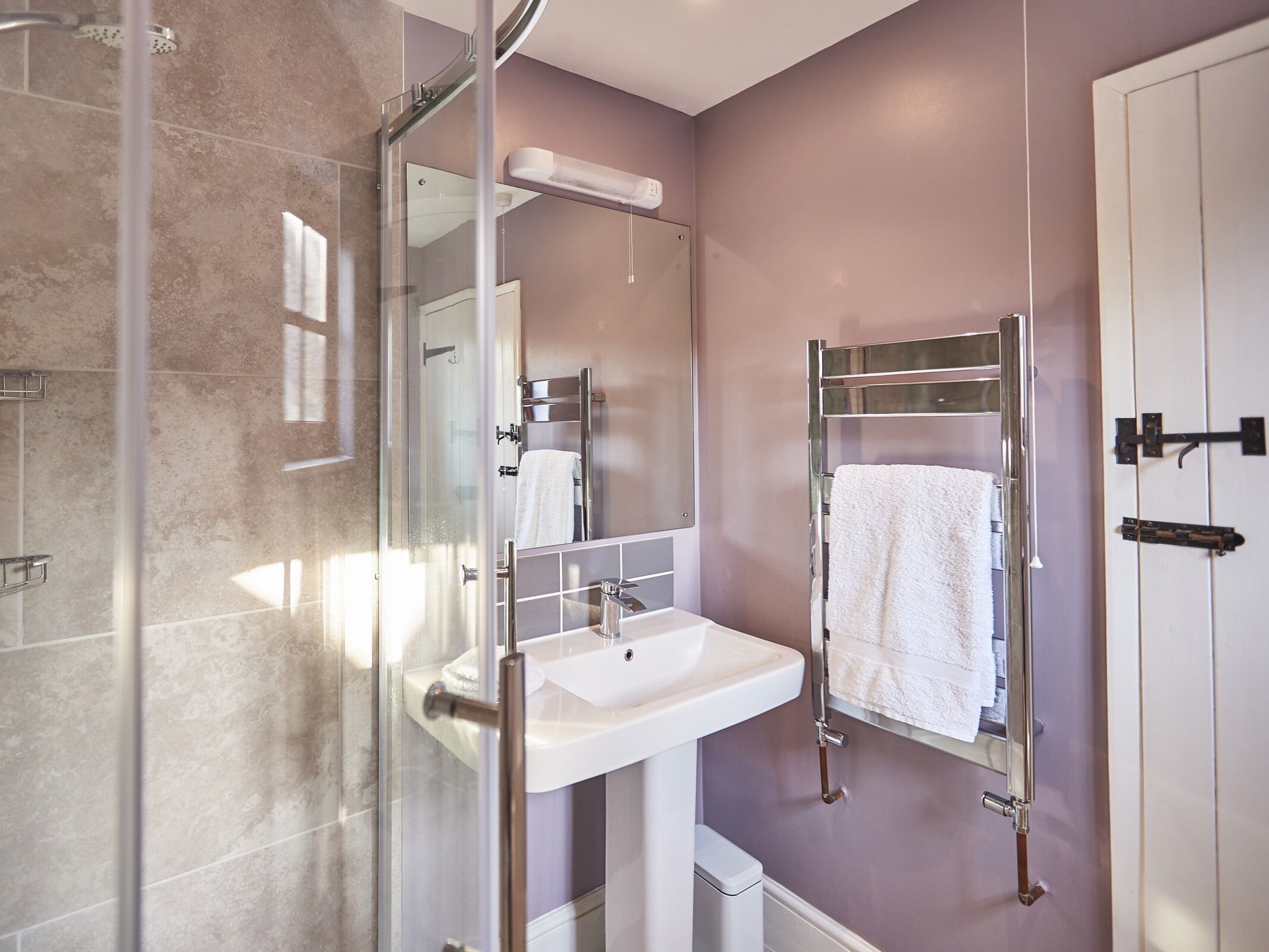 A modern bathroom with a glass shower enclosure, a white sink, and a towel rack.