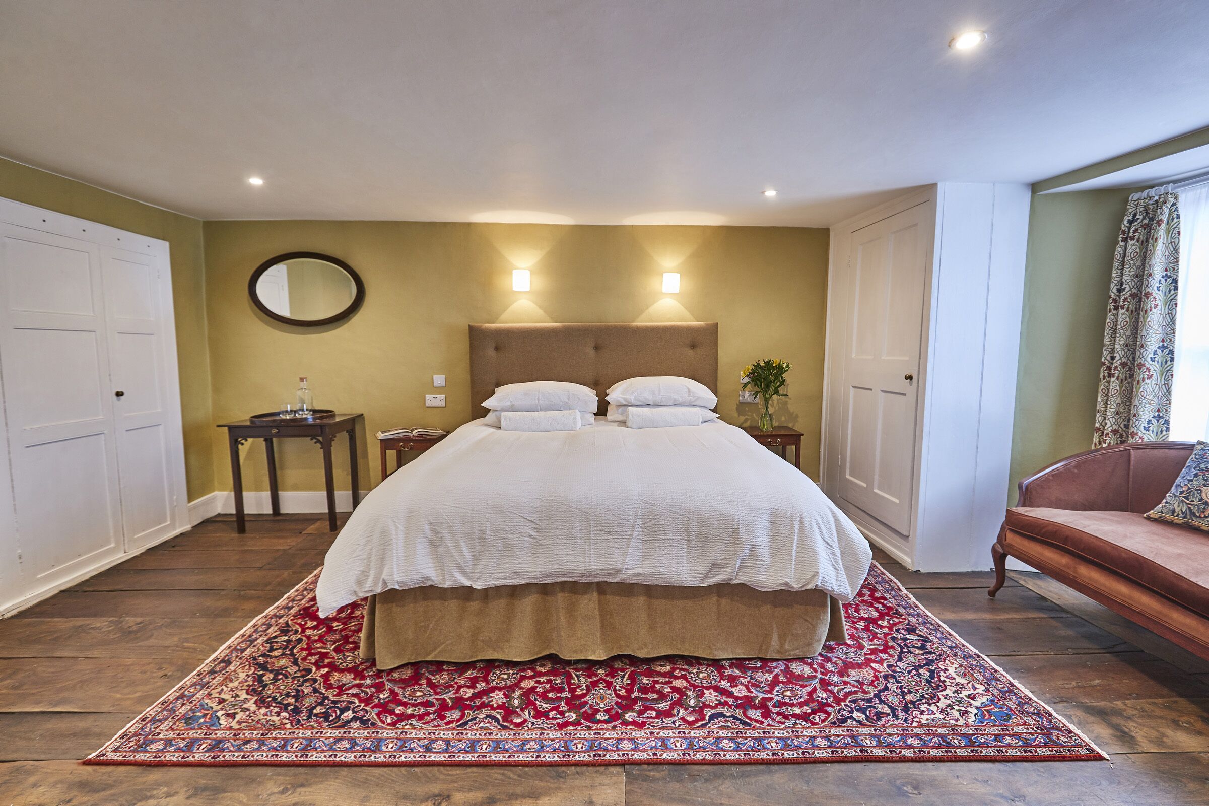 Ein Schlafzimmer mit einem großen Bett, zwei Nachttischen, einem runden Spiegel und einem Teppich mit rotem Muster.