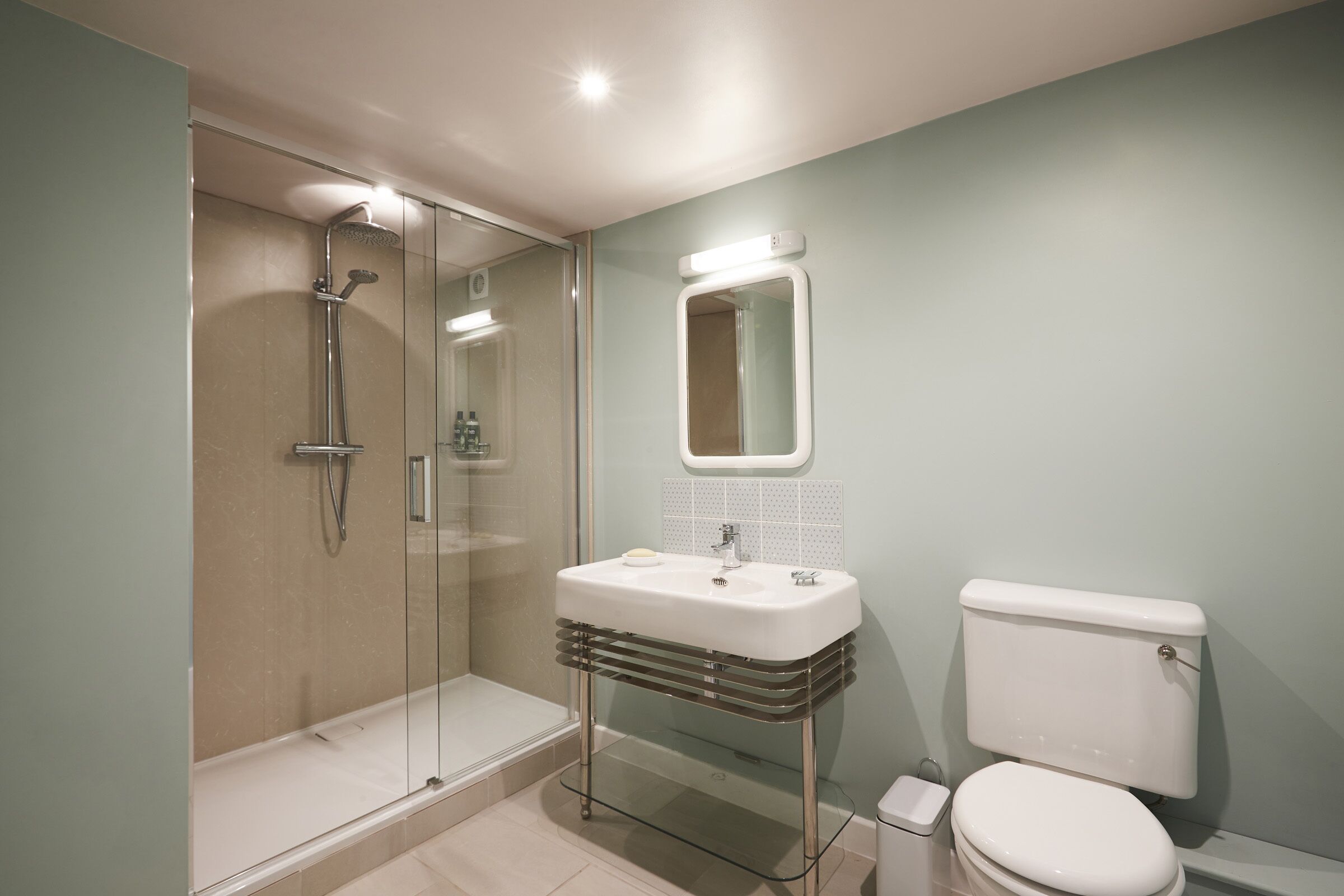 A modern bathroom with a glass-enclosed shower, a white sink with a mirror above it, and a white toilet.