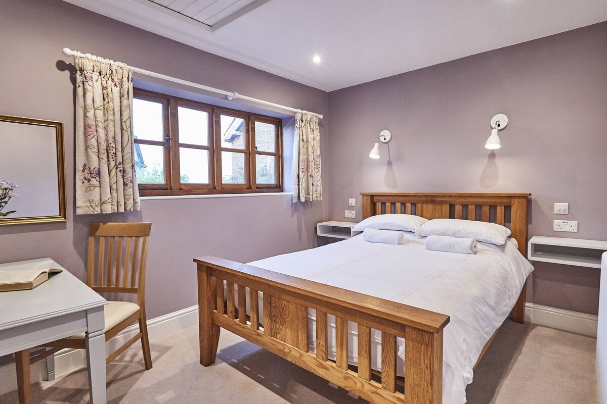 A bedroom with a wooden bed, a desk, a chair, and a window with curtains.