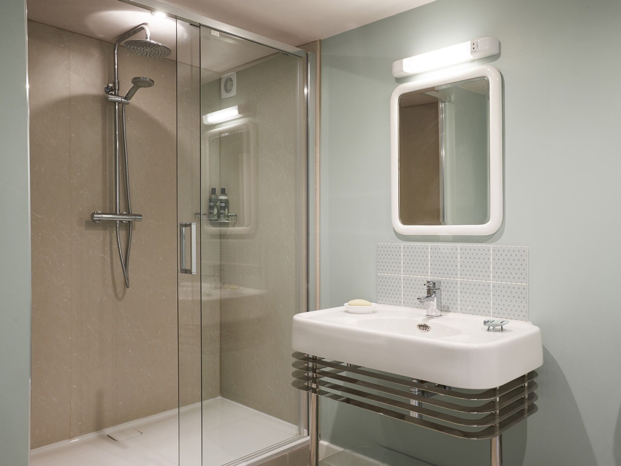 Ein modernes Badezimmer mit einer gläsernen Dusche, einem weißen Waschbecken mit Chromarmatur und einem Spiegel darüber.