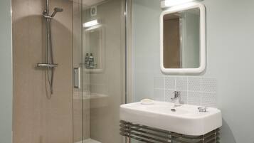 Ein modernes Badezimmer mit einer gläsernen Dusche, einem weißen Waschbecken mit Chromarmatur und einem Spiegel darüber.