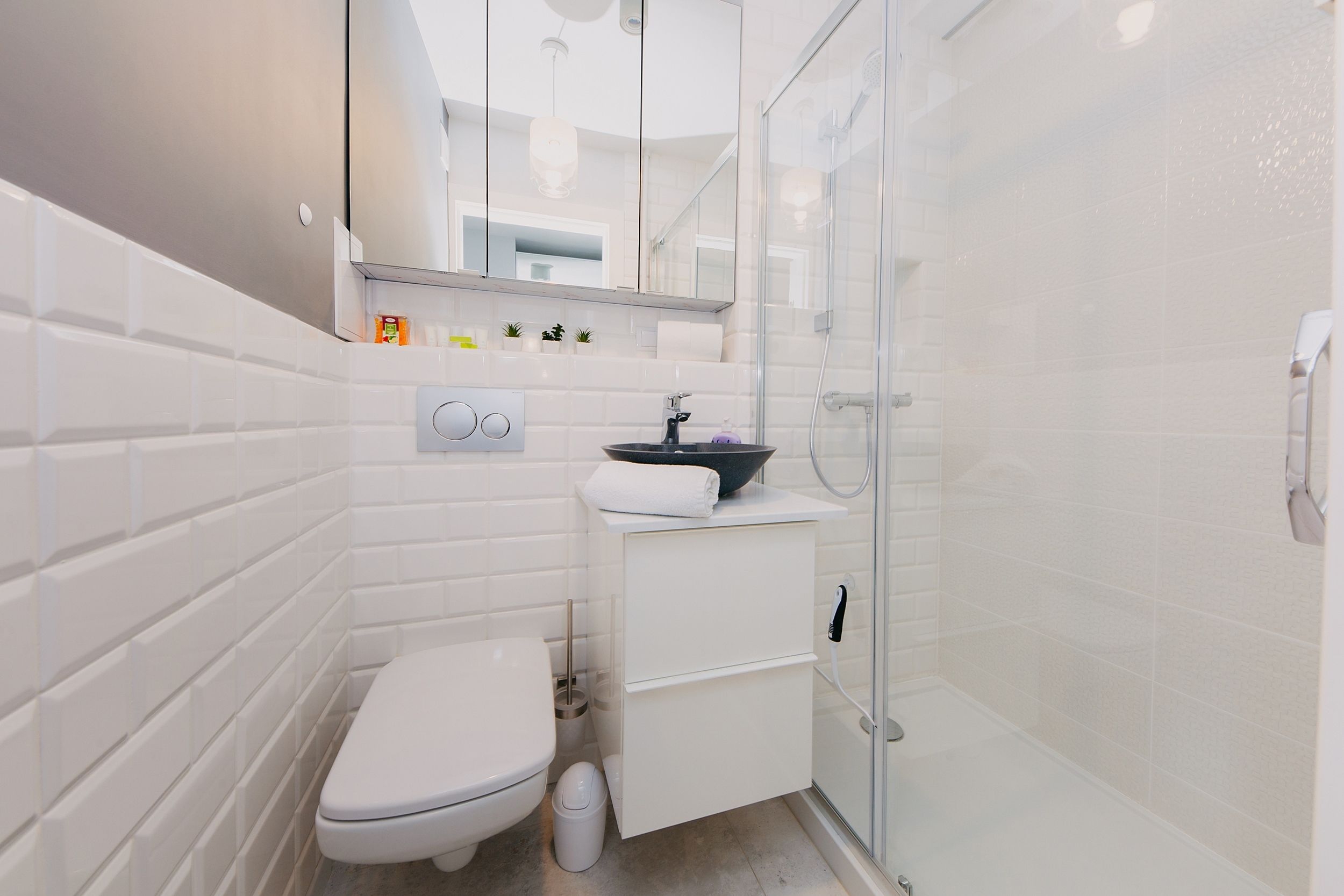 Un baño pequeño con inodoro blanco, lavabo con recipiente negro y mampara de ducha de vidrio.