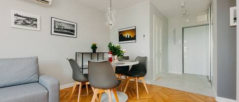 Una sala de estar moderna con un sofá gris, una mesa de comedor con sillas, una araña y un piso de madera con patrón de espiga.
