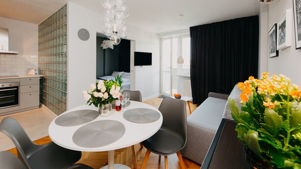 Een moderne keuken met een inbouwoven, een eethoek met een ronde tafel en stoelen, en een zithoek met een bank en een groot raam.