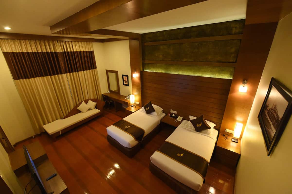 A hotel room with two beds, a sofa, a desk, and a large window with curtains.