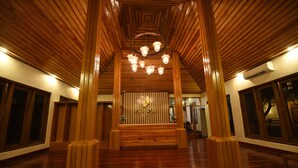 A spacious lobby with wooden flooring, a central seating area, and a decorative ceiling with hanging lights.