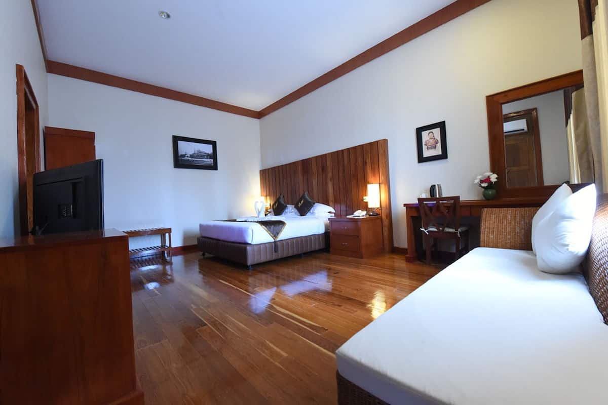 A hotel room with a wooden floor, a bed, a desk with a chair, a television, and a mirror.