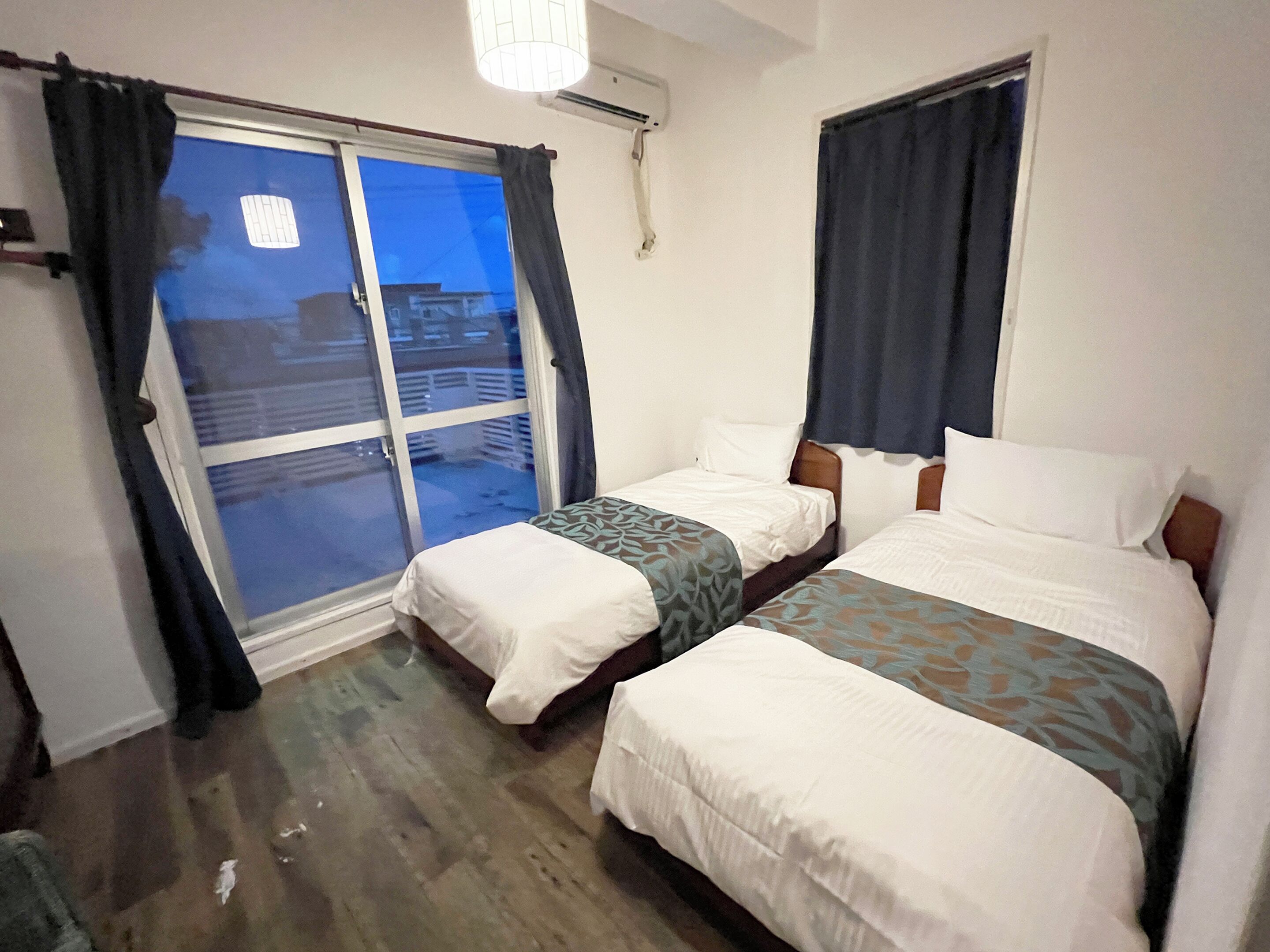 A hotel room with two beds, a sliding glass door, and a ceiling fan.