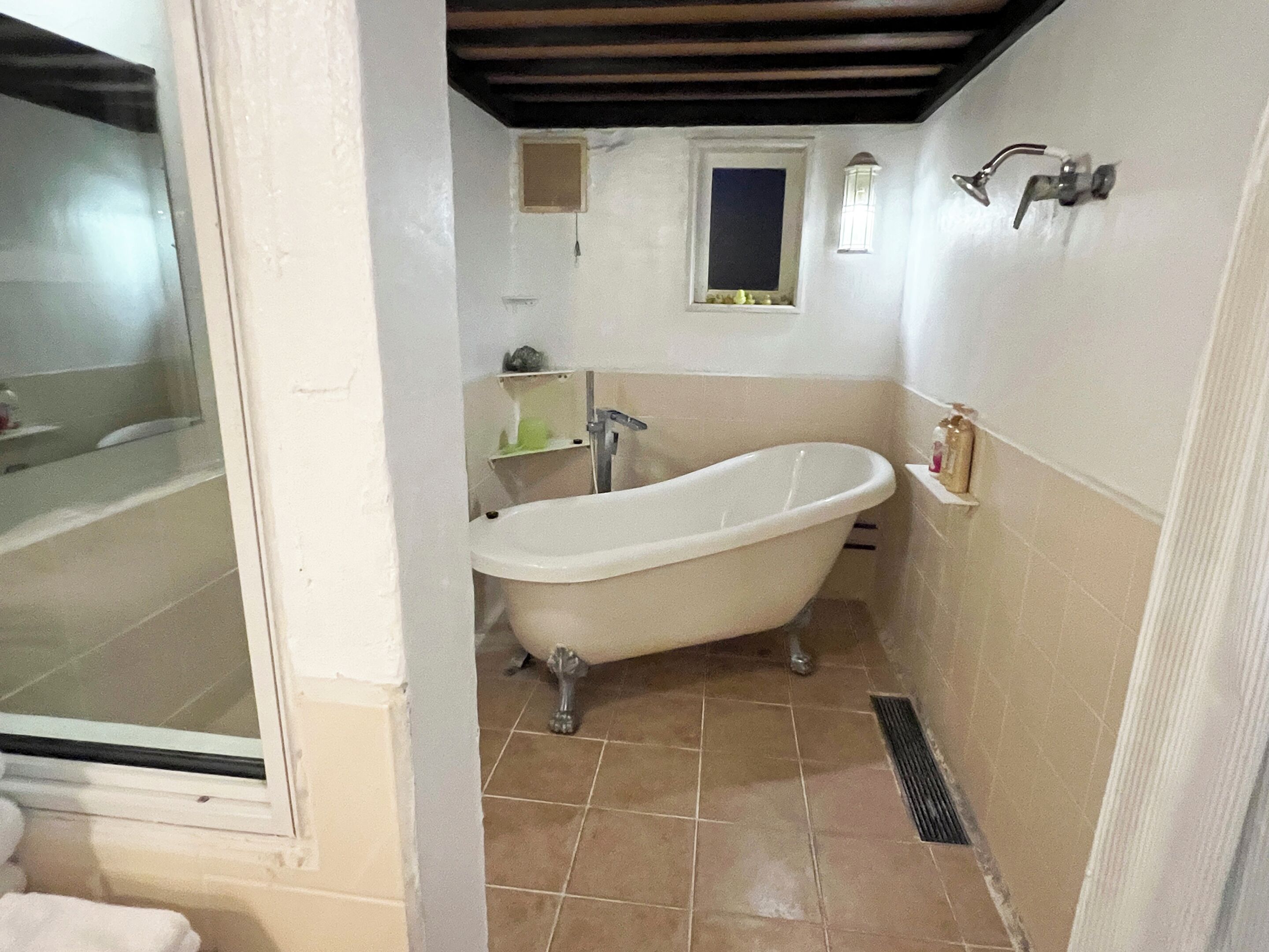 A bathroom with a freestanding bathtub, a window, and a small mirror.