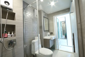 A modern bathroom with a glass shower enclosure, a toilet, a sink, and a mirror. - Neveu Premier Residence (Bangkok)
