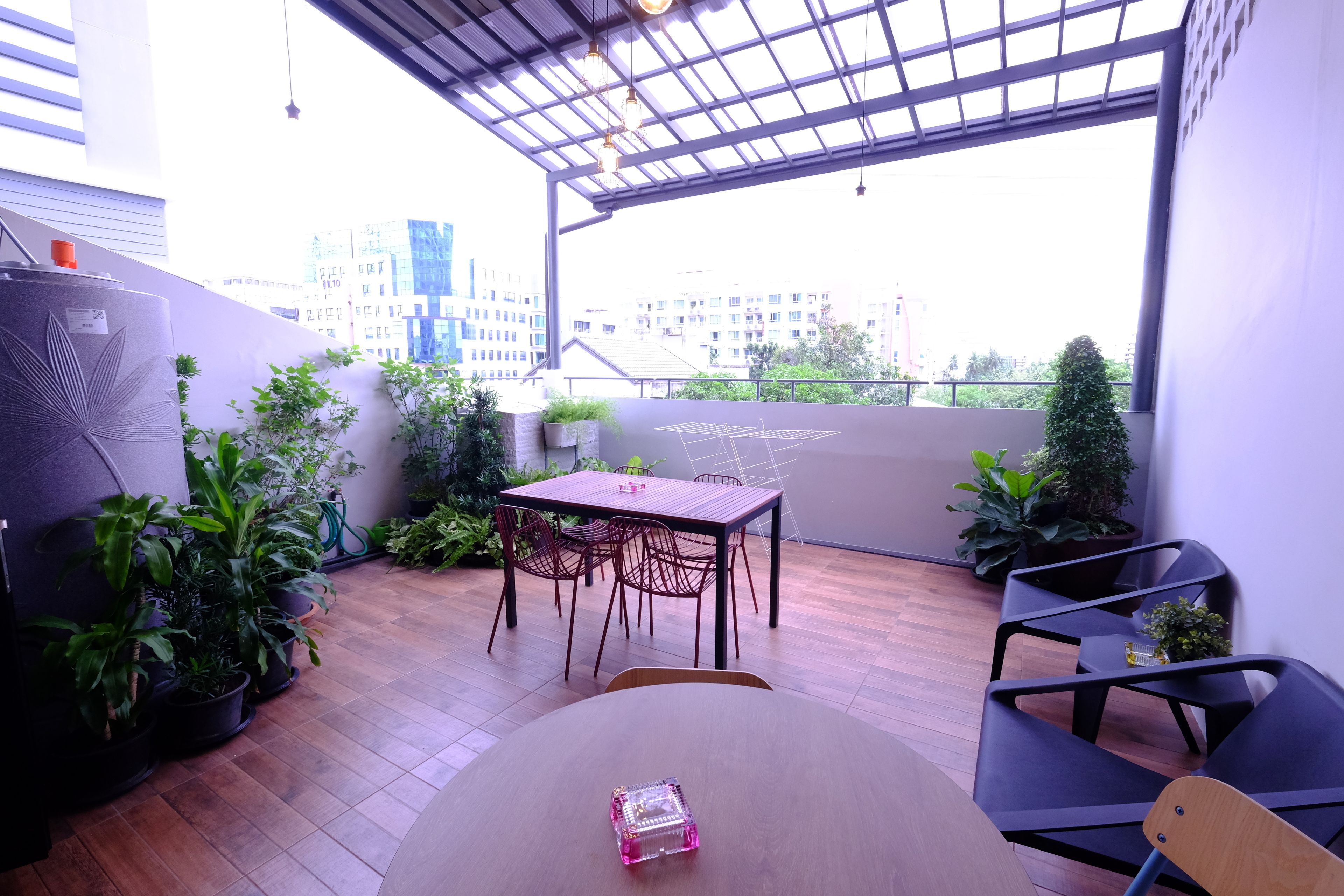 A modern outdoor patio with a wooden table and chairs, surrounded by potted plants and a view of city buildings.