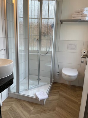 A modern bathroom with a glass-enclosed shower, a white toilet, and a sink with a beige basin. - Dom-Hotel (Osnabrueck)
