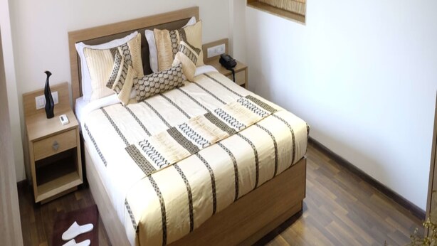 Una cama bien hecha con colcha a rayas, cabecera de madera y mesita de noche con lámpara y teléfono.