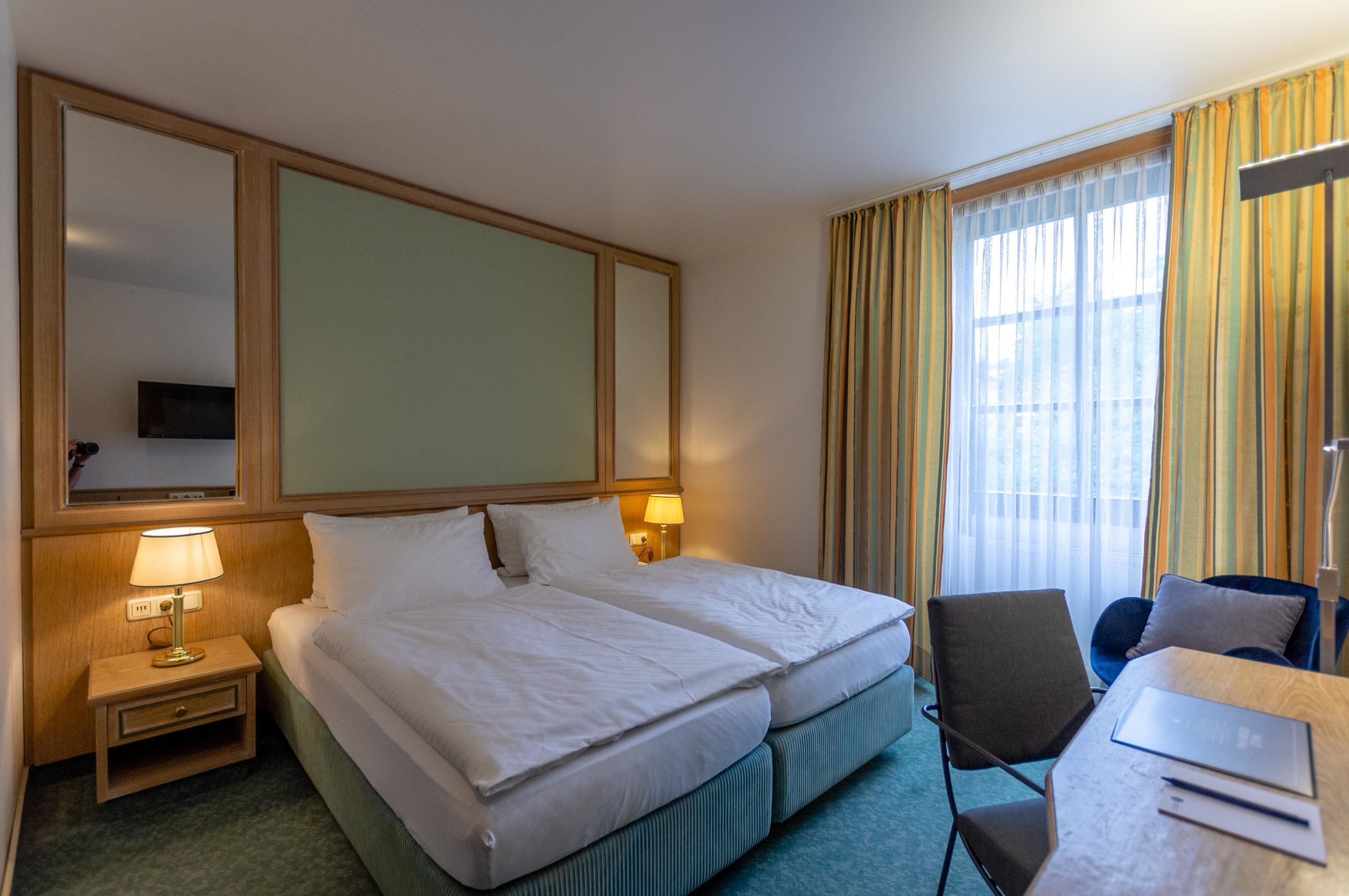 Una camera d'albergo con un letto matrimoniale, una scrivania con una sedia, una lampada e un televisore a parete.