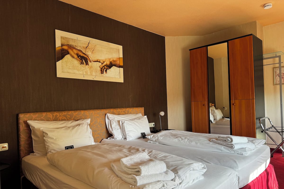 A hotel room with two beds, a large mirror, and a painting on the wall.