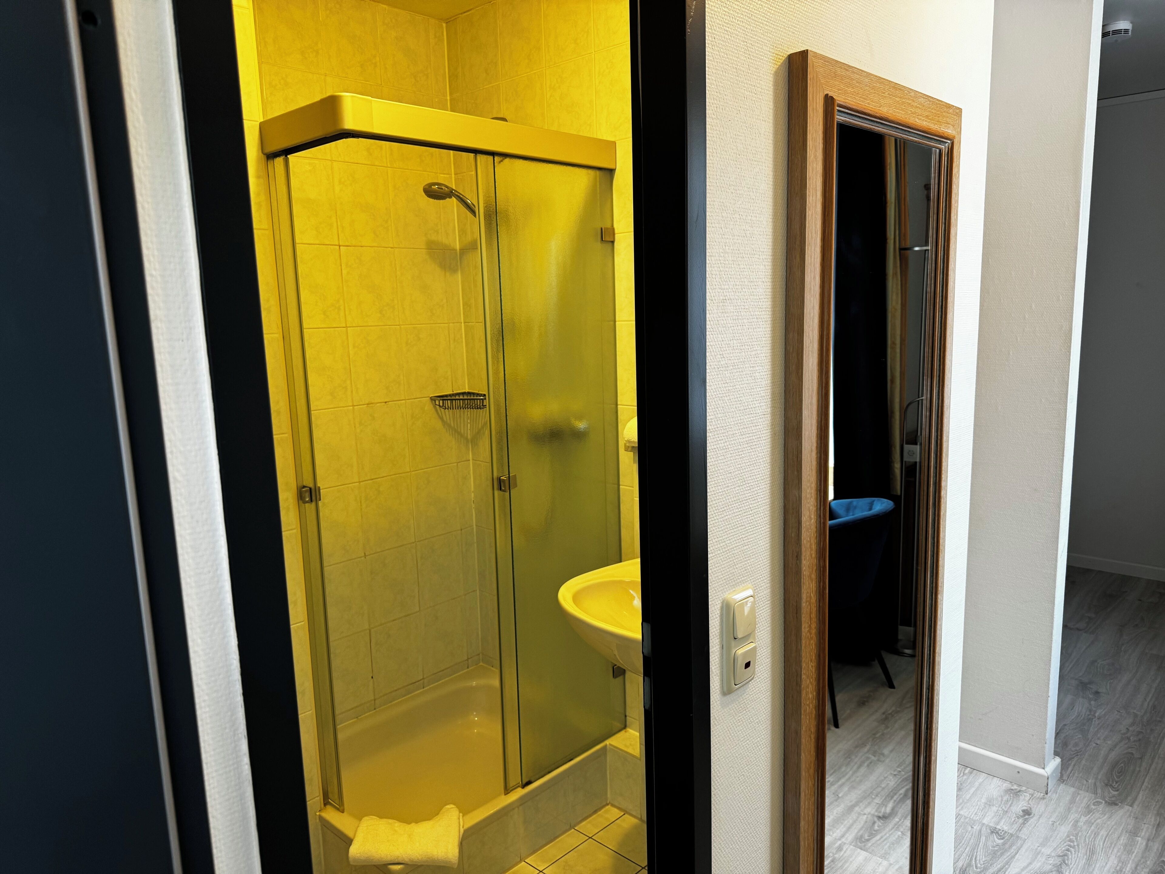 A modern bathroom with a glass-enclosed shower, a white sink, and a wooden door frame.