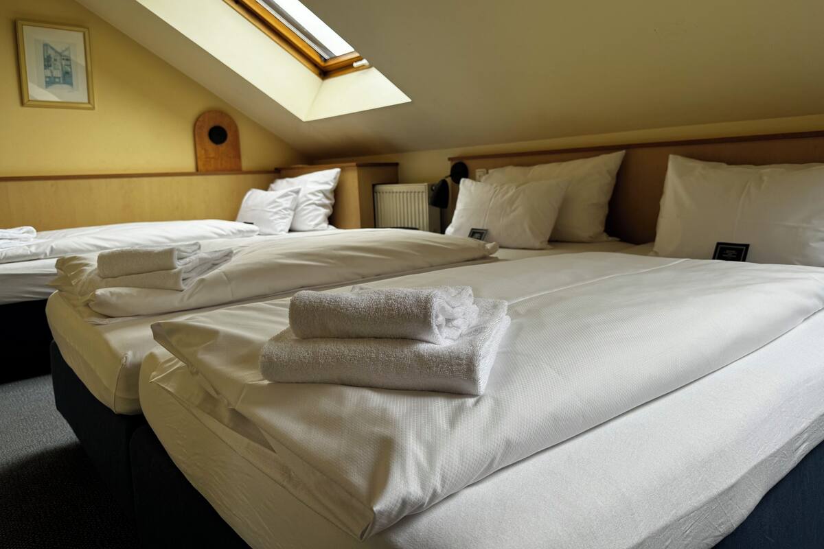 A hotel room with two beds, a skylight, and a framed picture on the wall.