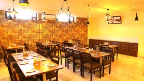 Un restaurant doté de nombreuses tables et chaises, d'un papier peint à motifs et de différents types de luminaires suspendus.