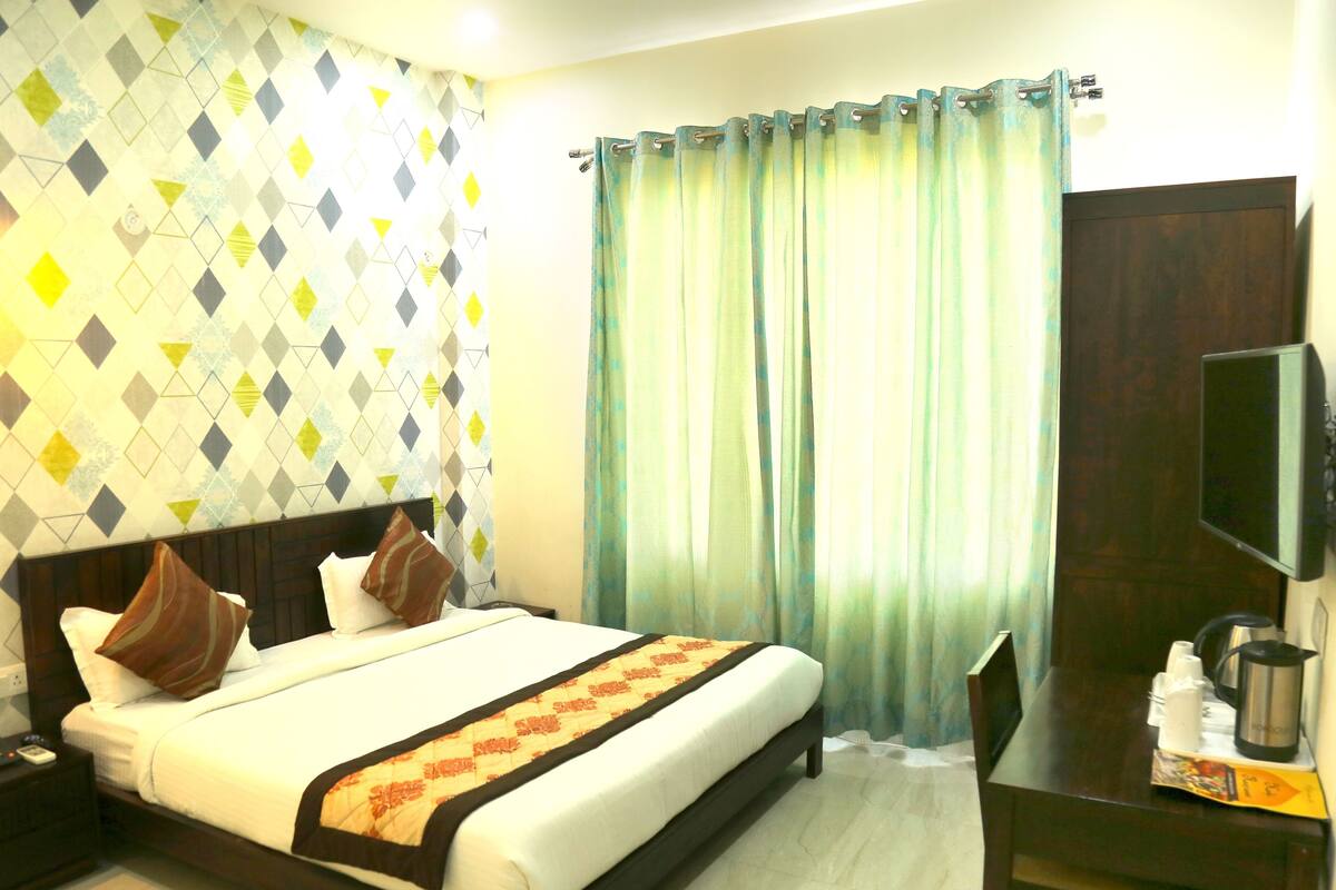 Una habitación de hotel con cama, cortinas, televisión y escritorio con cafetera.