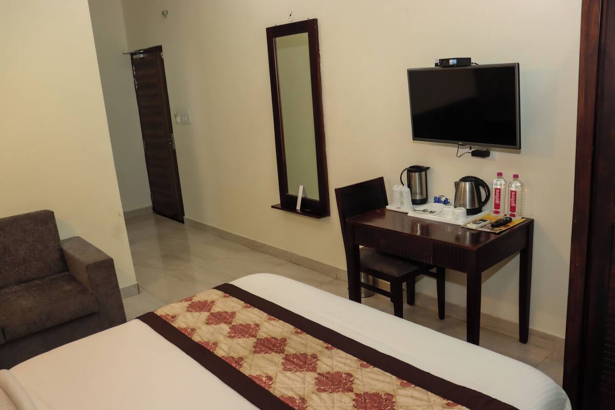 Una habitación de hotel con cama, escritorio, silla, televisión y espejo.